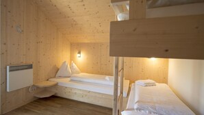 Una habitación tipo cabaña de madera con literas, un calentador y una lámpara fijada a la pared.