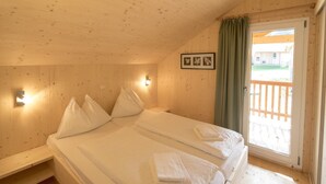 Una habitación de madera con una cama, una mesita pequeña, una lámpara de pared y una ventana con cortina.