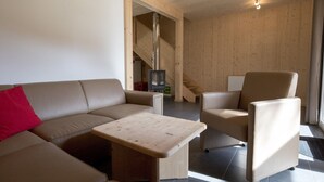 Un salón moderno con sofá, sillón y mesa de centro, paredes de madera y una escalera.