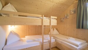 Habitación con literas de madera, ropa blanca de cama, una escalera y una ventana pequeña con cortinas.
