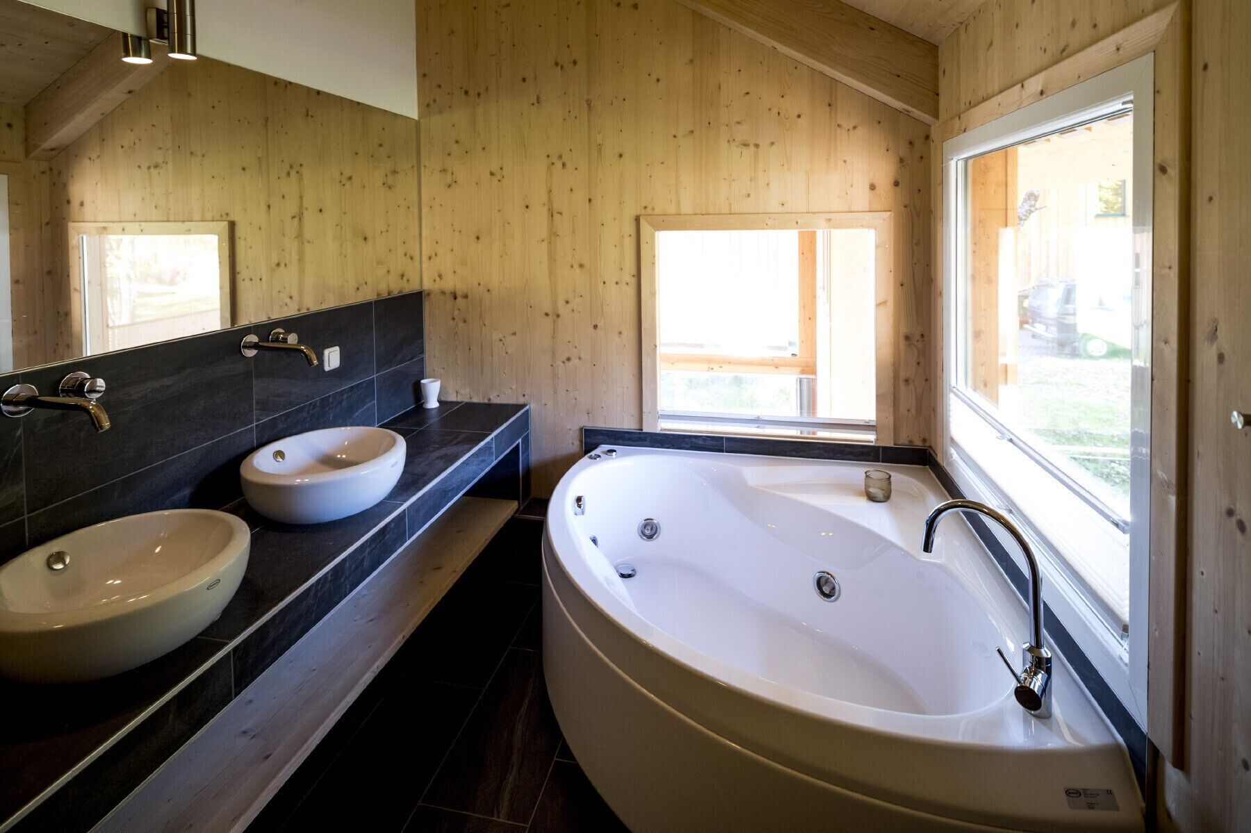 A modern bathroom with two sinks, a bathtub, and a large window.