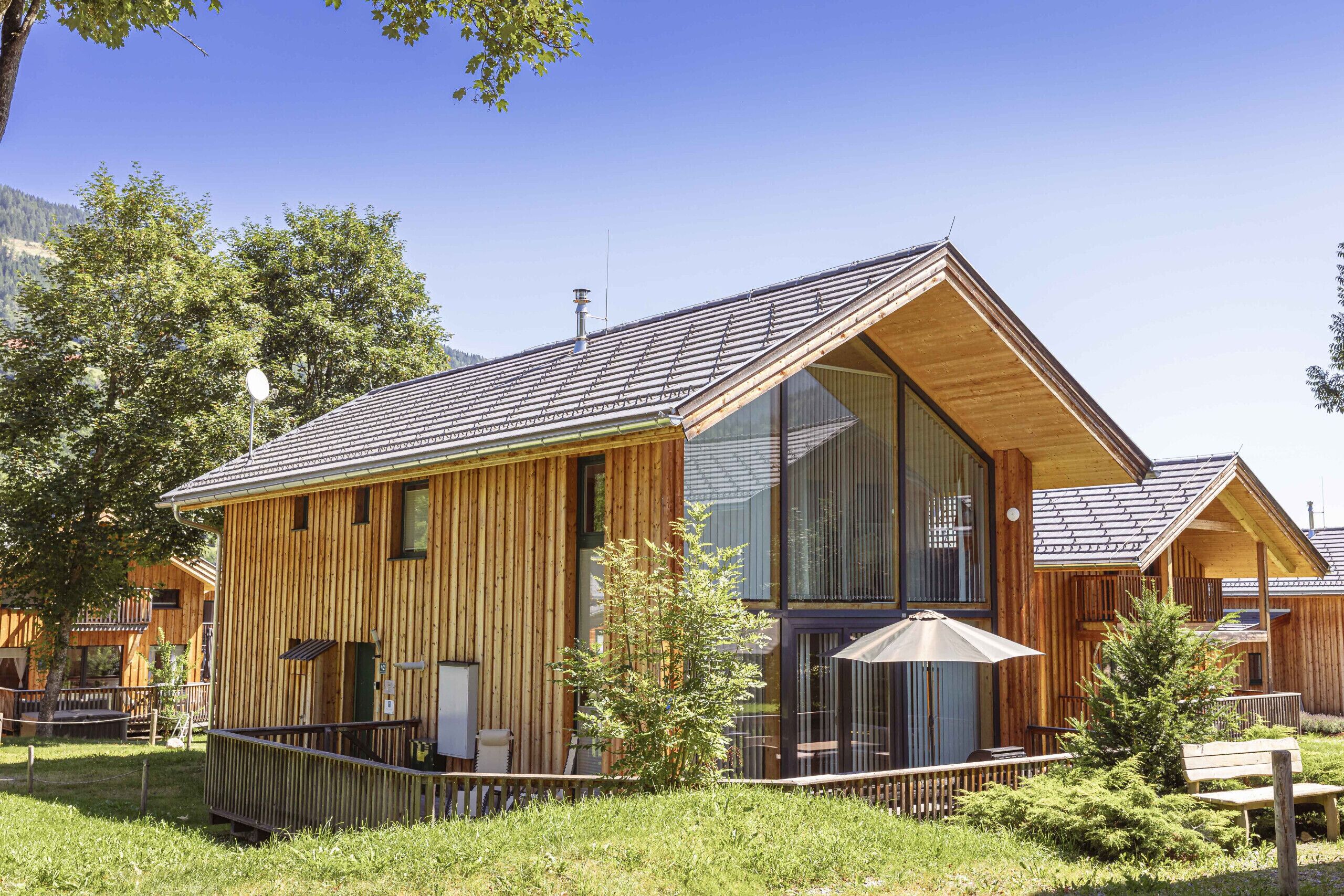 A wooden cabin with large windows, a balcony, and a grassy yard.