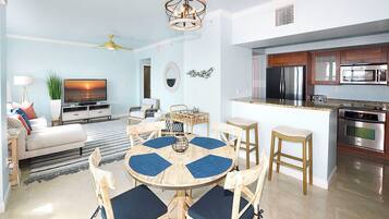 Un salon moderne comprenant un téléviseur, un canapé et un coin repas avec des chaises et une table.