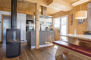 A wooden interior with a central fireplace, a kitchen area, and a dining space with a bench.