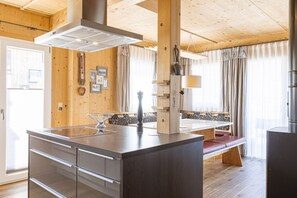 A wooden interior with a kitchen island, wooden beams, a bench, and a view through large windows.