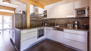 A modern kitchen with wooden ceiling beams, stainless steel appliances, and white cabinetry.