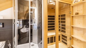 A modern bathroom with a glass-enclosed shower, a wooden sauna, and a visible toilet.
