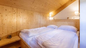 A wooden room with two beds, wooden walls, and a sloped ceiling.