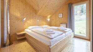 Puinen mökkimainen makuuhuone, jossa on kaksi sänkyä, ikkuna, josta on näkymä ulos, ja sisäänrakennettu hylly.