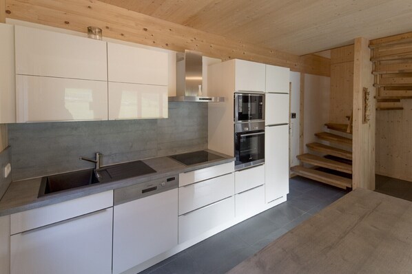 A modern kitchen with white cabinetry, a stainless steel range hood, a double oven, and a built-in microwave.