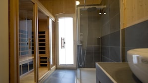Un baño moderno con cabina de ducha de vidrio, tocador de madera y puerta corrediza de vidrio que da a un balcón.