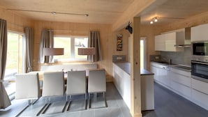 Una cocina moderna con armarios blancos, horno empotrado y comedor con mesa y sillas.