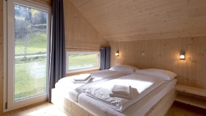 Un dormitorio con un ventanal grande, paredes de madera y una cama con almohadas y una colcha.