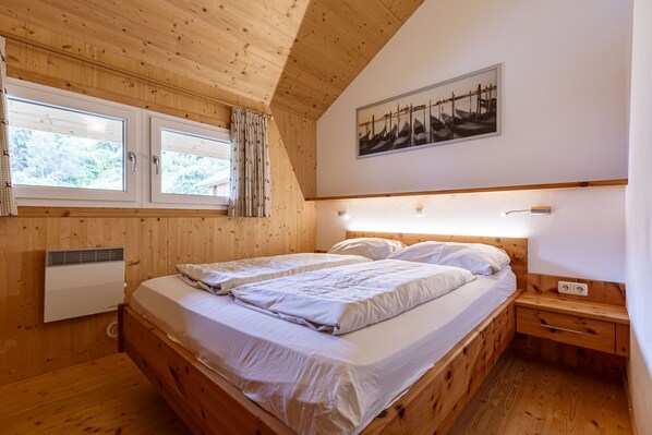 Un dormitorio con paneles de madera, dos camas, una ventana con cortinas, un calentador fijado a la pared y un cuadro sobre las camas.