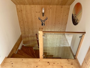 Eine Holztreppe mit Glastrennwand, eine an der Wand befestigte Dekoration mit Hirschgeweih und ein gerahmtes Bild.