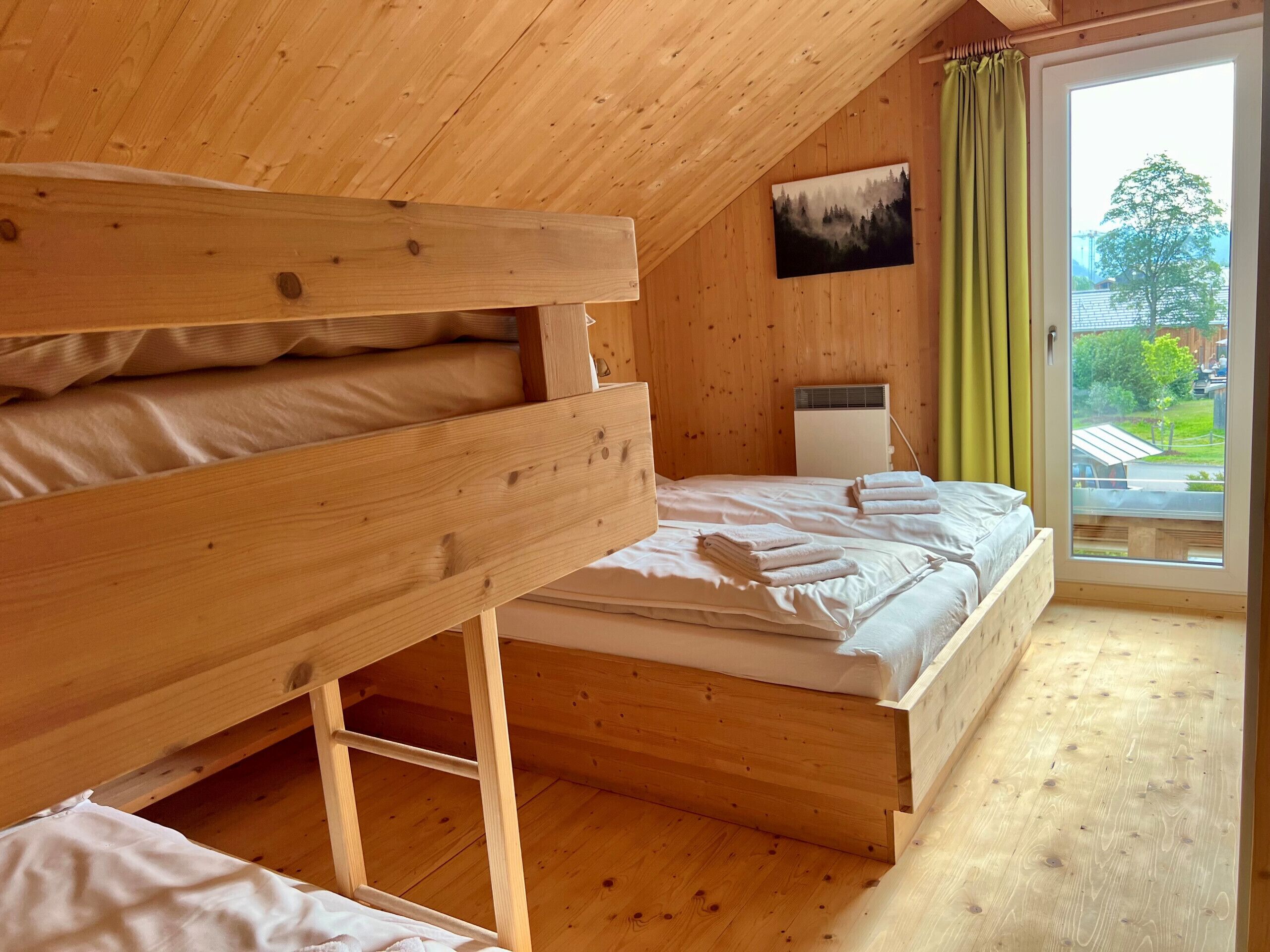A wooden room with bunk beds, a bed, a radiator, and a window with a view.
