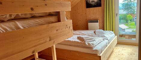 A wooden room with bunk beds, a bed, a radiator, and a window with a view.