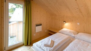 Ein Holzhäuschen-Zimmer mit zwei Betten, einem Fenster mit Vorhängen, einem kleinen Heizgerät und einer Holzbank.