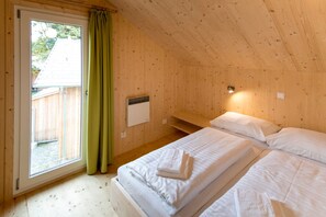 Ein Holzhäuschen-Zimmer mit zwei Betten, einem Fenster mit Vorhängen, einem kleinen Heizgerät und einer Holzbank.