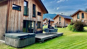 Eine Holzhütte mit einer Terrasse, einem Whirlpool und einem Essbereich mit Gartenmöbeln.