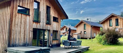 Una cabaña de madera con terraza, jacuzzi y comedor con mobiliario exterior.