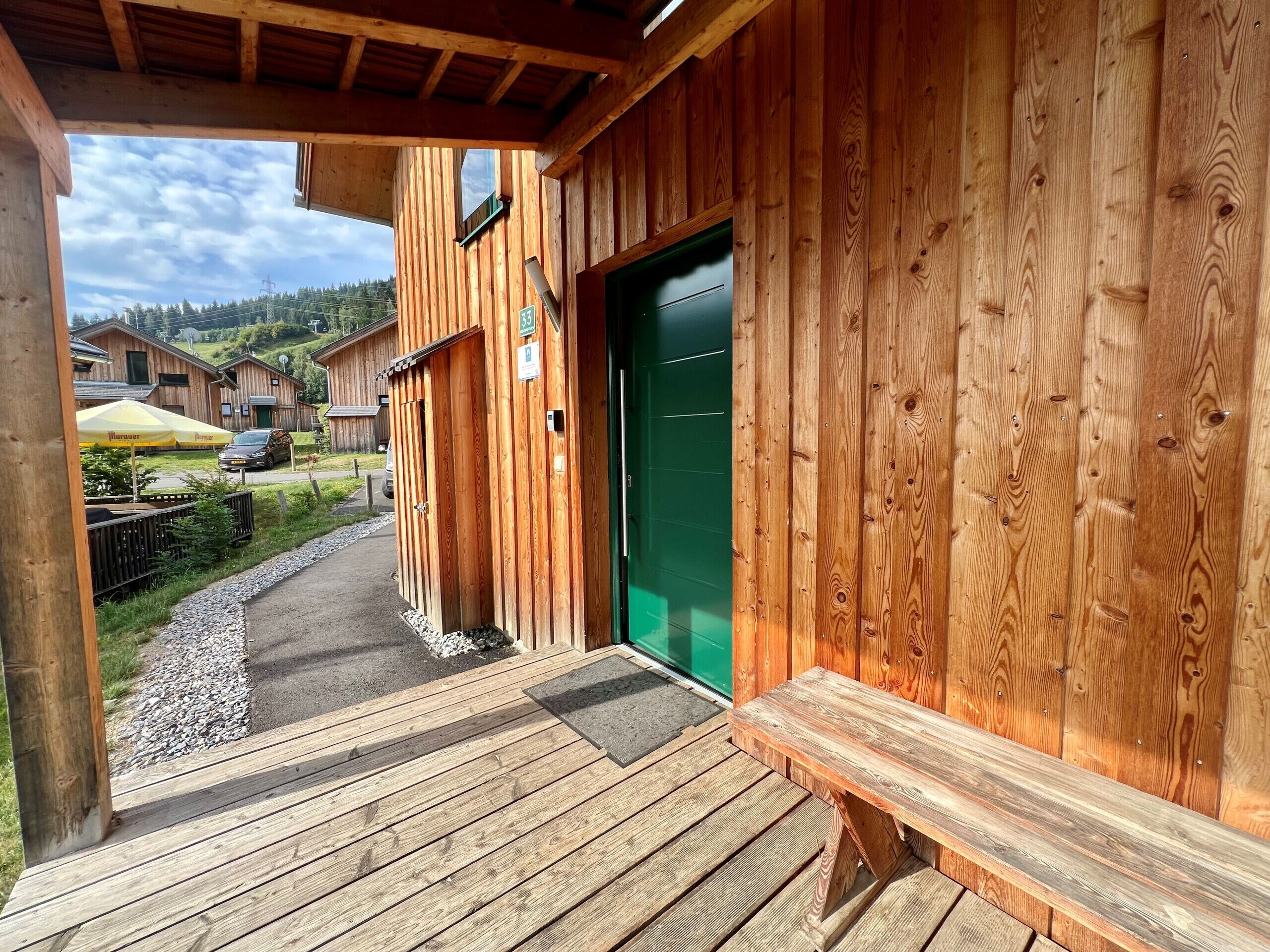 Ein Holzhaus mit grüner Tür, einer Holzterrasse und Blick auf die Umgebung.