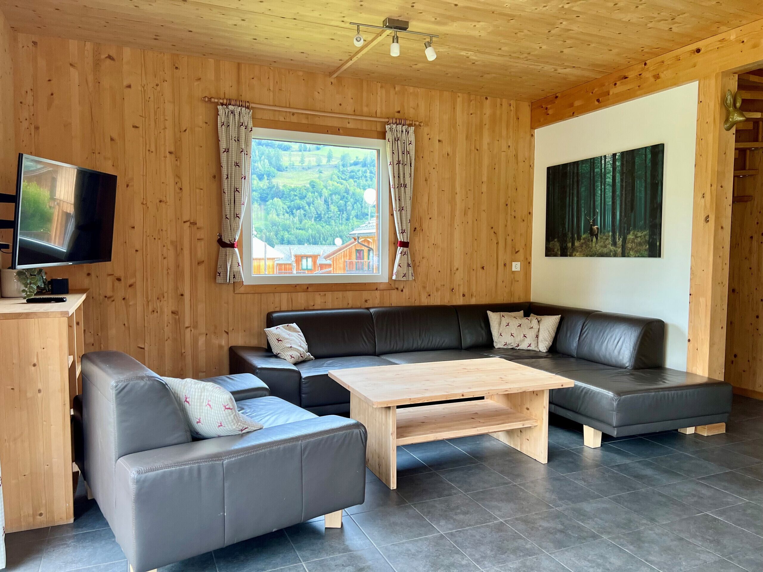 Ein modernes Wohnzimmer mit Holzboden, einem Flachbildfernseher, einer Sofagarnitur, einem Couchtisch und einem Fenster mit Vorhängen.
