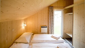 A room with wooden walls, two beds with white linens, a window with a curtain, and a wall-mounted air conditioner.