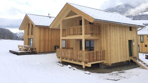 Una cabaña de madera con balcón, un espacio de estar al aire libre cubierto y un paisaje cubierto de nieve.