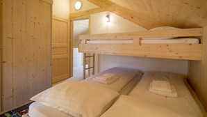 Habitación con dos literas de madera, una escalera, una puerta y un ventanal pequeño.