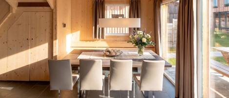 Un interior de madera con una mesa de comedor, sillas y un ventanal con cortinas.