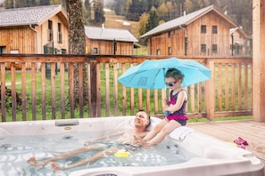 En træterrasse med jacuzzi, omgivet af træhytter.