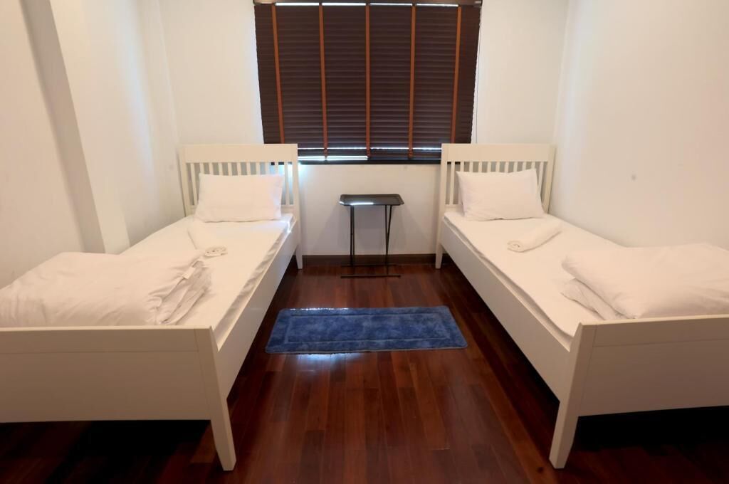 Een kleine, schone kamer met twee eenpersoonsbedden, een tafeltje en een raam met zonwering.
