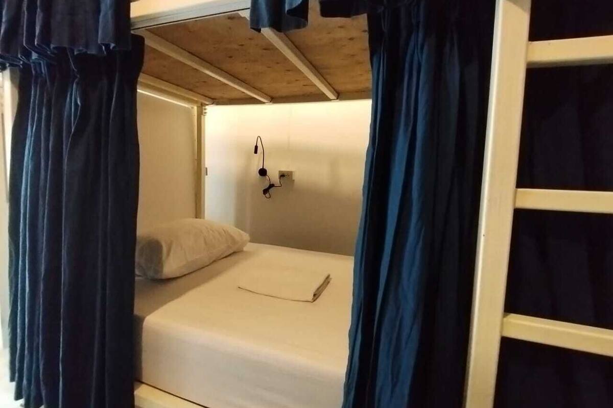Una cama litera con un colchón blanco y una almohada. Hay un pequeño estante con un par de gafas y un libro.