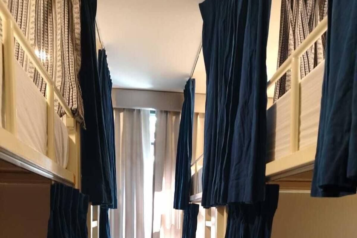 Un pasillo estrecho con literas a ambos lados, suelo de baldosas y una ventana con cortinas.
