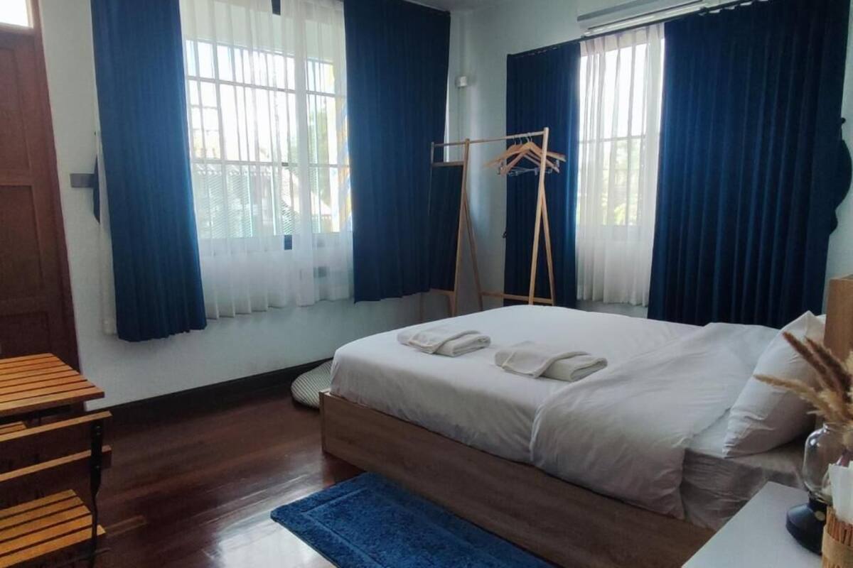 Un dormitorio con una cama, una mesa de madera, un tapete azul y una ventana con cortinas.