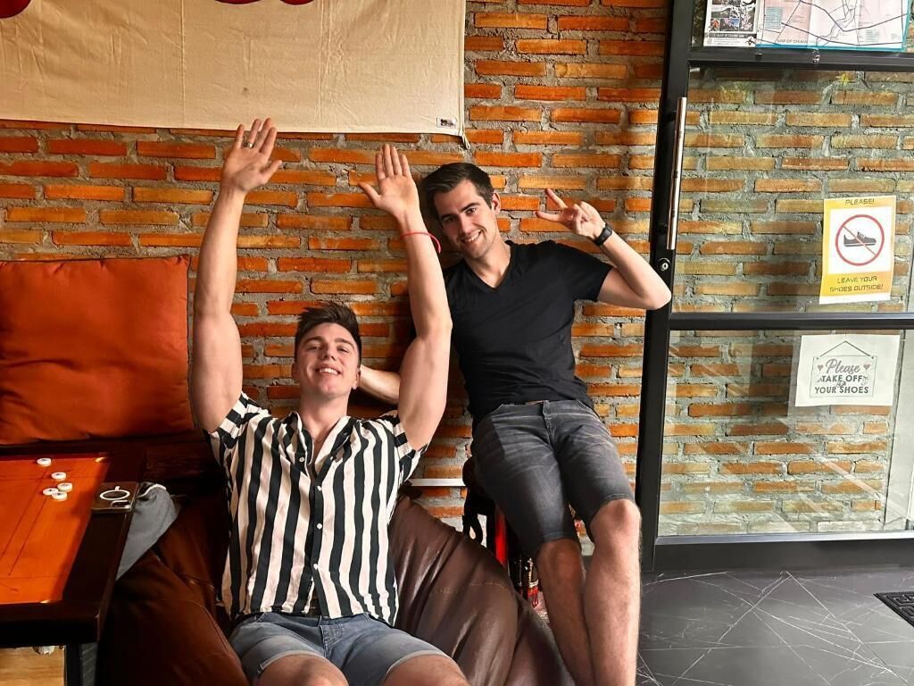 Zwei Personen sitzen auf einem braunen Ledersofa in einem Raum mit Backsteinwand und Glastür.