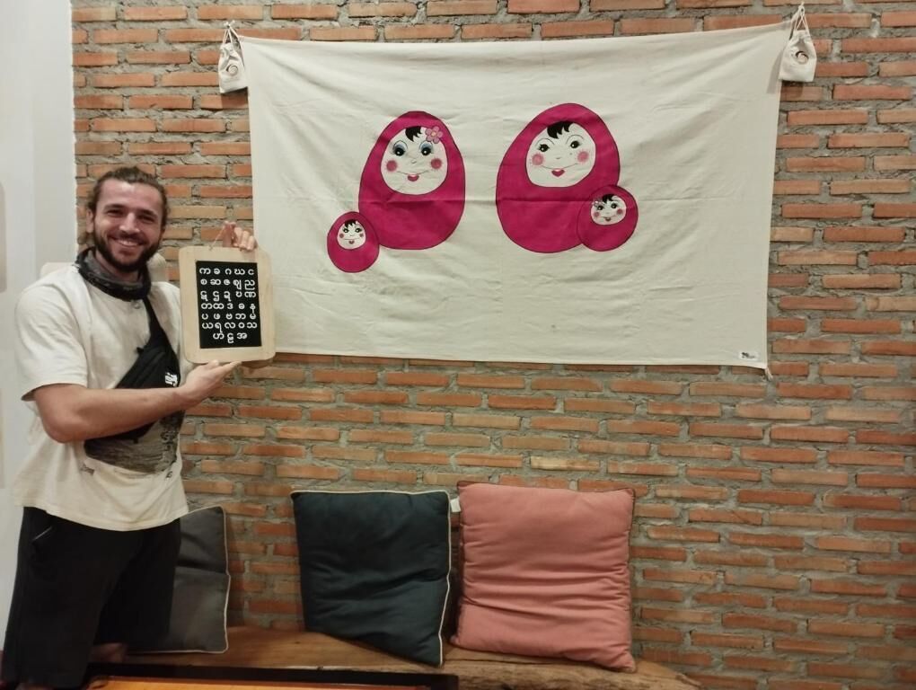 Une personne tenant une pancarte représentant un personnage de dessin animé, debout devant un mur de briques sur lequel est accrochée une banderole blanche ornée de personnages de dessins animés.