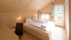 Un dormitorio de cabaña de madera con cama, almohadas, una mesita de noche y ventana con cortinas.
