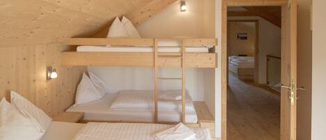 A bunk bed room with wooden walls and a sloped ceiling. There is a ladder attached to the bunk bed, and a door leading to another room.