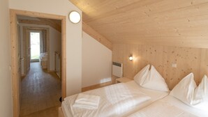 Une chambre avec un plafond en bois, un lit recouvert de draps blancs et un radiateur apparent.