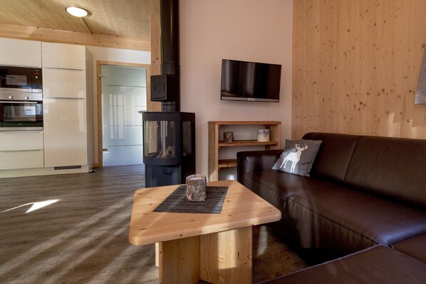 A cozy living room with a dark brown leather sofa, a wooden coffee table, and a television mounted on the wall.