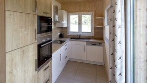 A compact kitchen with wooden cabinets, a built-in oven, a microwave, a sink, and a window with a view of the outdoors.