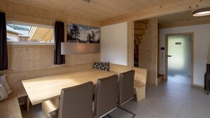 A wooden interior with a dining table, chairs, a painting, and a window.