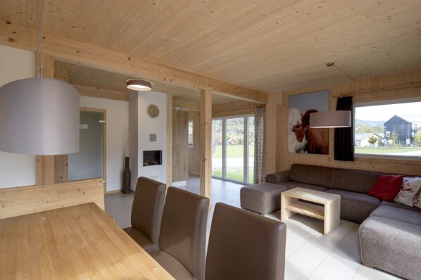 Amplia sala de estar con techo de madera, un conjunto de sofás, una mesa de comedor con sillas y un ventanal con vistas al exterior.