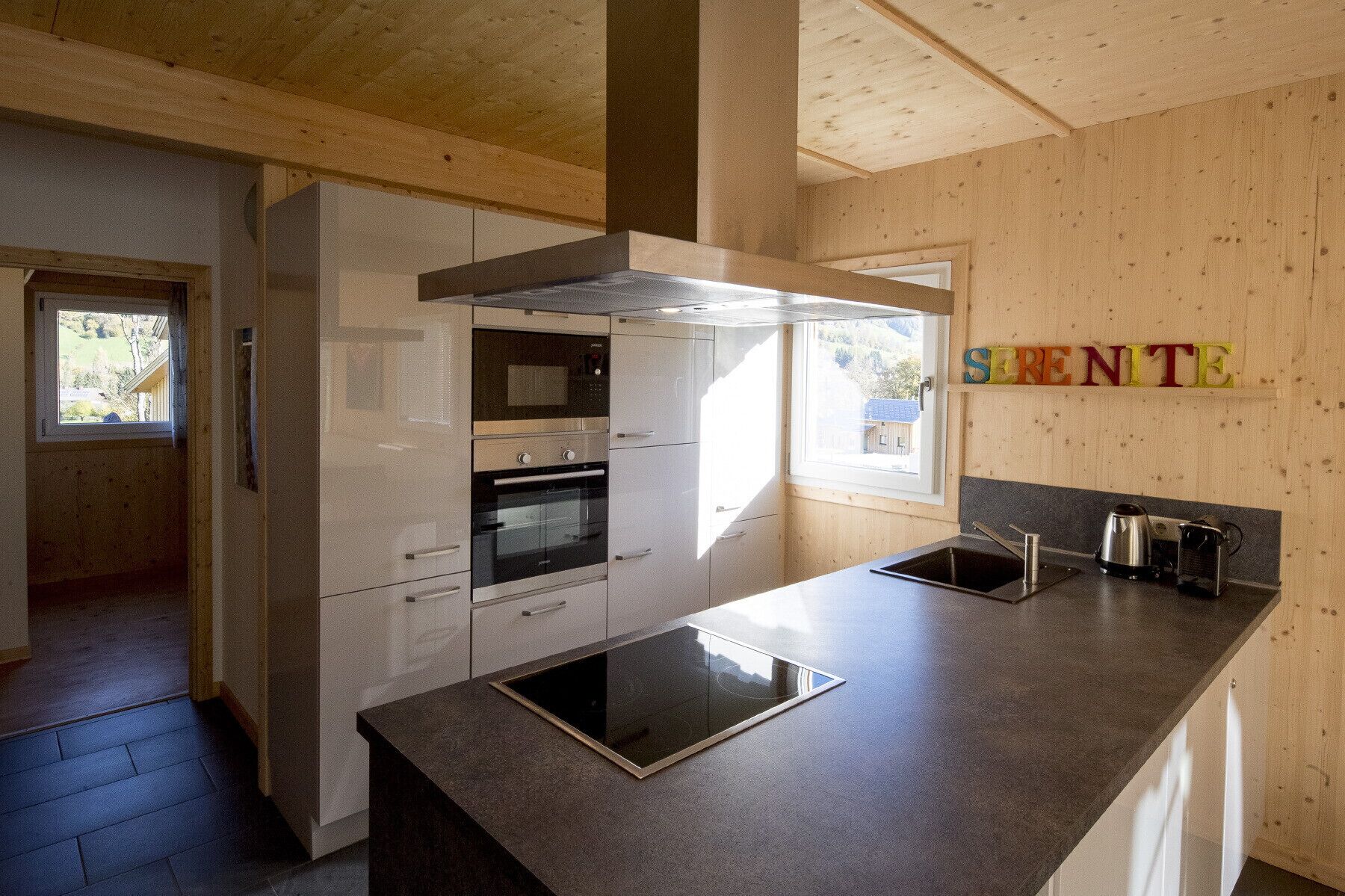 A modern kitchen with a large island, built-in ovens, and a wooden accent wall with the word "SERENITY".