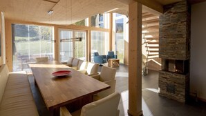 A modern interior with a wooden dining table, sofas, and a stone fireplace.