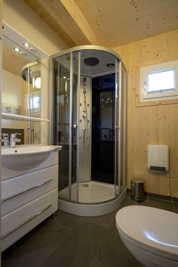 Un baño moderno con ducha de vidrio, lavamanos blanco con espejo y un inodoro.