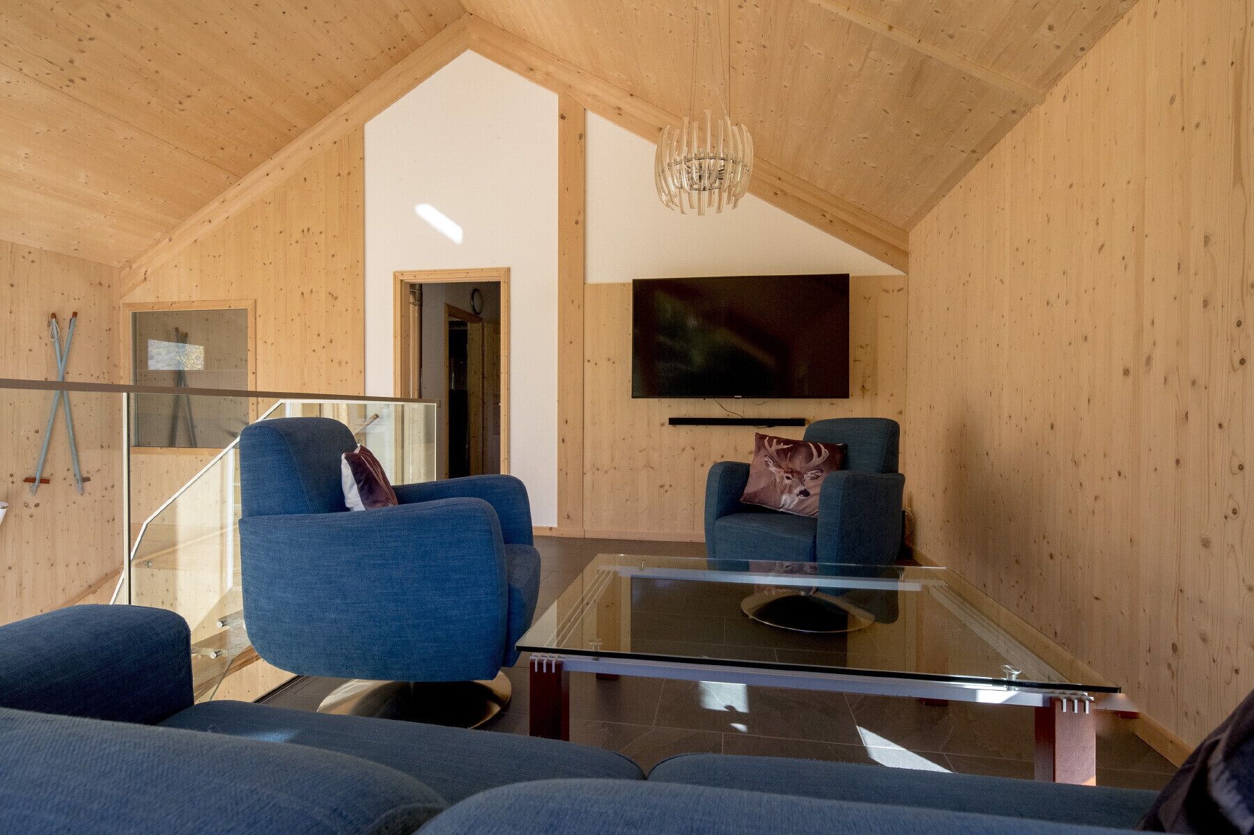 A cozy living room with two blue armchairs, a glass coffee table, and a mounted TV.
