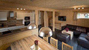 A modern interior with a wooden dining table, a sofa, and a kitchen area with appliances.